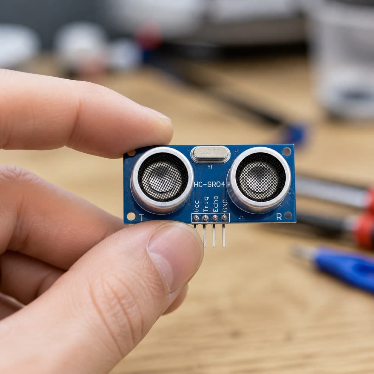 Sensor ultrasónico HC-SR04 sostenido entre los dedos para mostrar su escala aproximada.